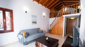 A living room with a sofa, coffee table, TV, wooden staircase, and a painting on the wall. - YIAYIA's Central Apartment (Simi Dodecanese)