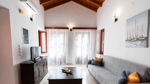 A living room with a sofa, a coffee table, a TV on a cabinet, and a painting on the wall. - YIAYIA's Central Apartment (Simi Dodecanese)