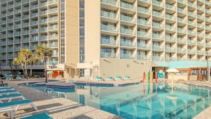 A hotel pool area with multiple lounge chairs, a pool, and a building with balconies. - Spacious 3 Bedroom Oceanview Condo at Sand Dunes Resort (Myrtle Beach)