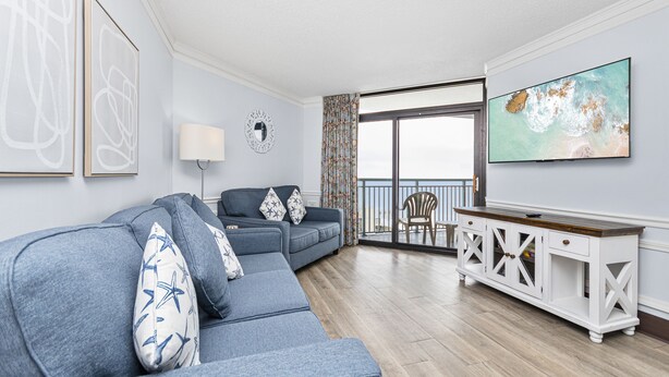 A living room with a grey sofa, a white console table, and a large window with a view of the ocean. - Spacious 3 Bedroom Oceanview Condo at Sand Dunes Resort (Myrtle Beach)