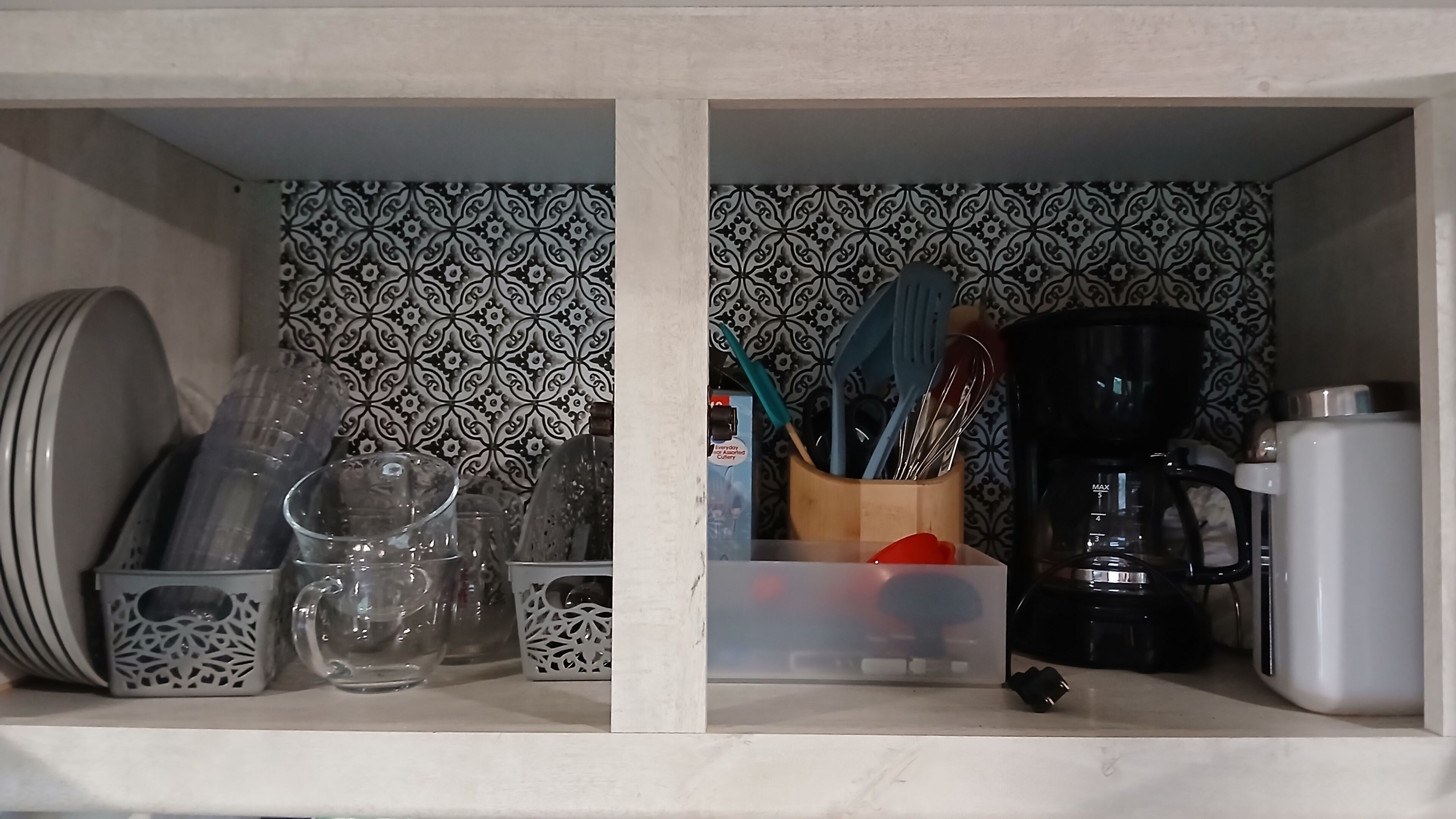 A kitchen shelf with dishes, glasses, a coffee maker, and utensils.