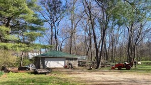 A single-story house with a green roof, a covered porch, and a yard with a tractor. - Cozy Camper in Villa Ridge (Villa Ridge)