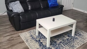 Un salon avec un canapé en cuir noir, une table basse blanche et un tapis à motifs.