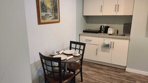 Un coin repas avec une table dressée pour deux personnes, un tableau accroché au mur et une petite cuisine équipée de placards et d’appareils électroménagers.