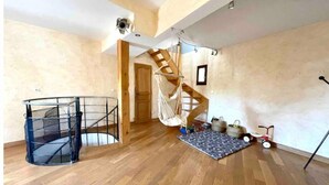 Une pièce spacieuse avec un escalier en bois, une chaise en métal noir et un hamac.