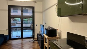 A modern living room with a large TV, wooden flooring, and a sliding glass door leading to a balcony.