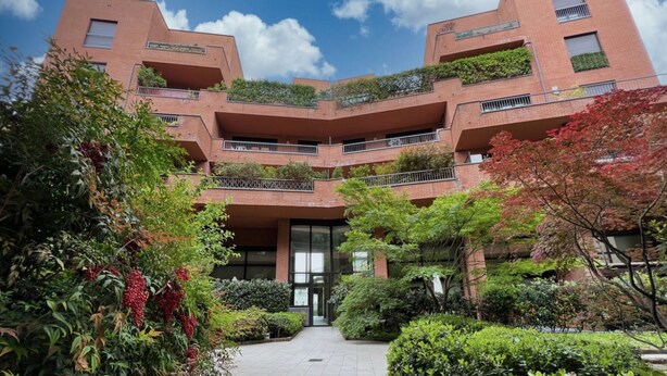 A multi-story building with a central courtyard, surrounded by lush greenery and trees.