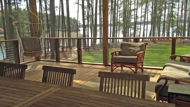 A wooden deck with a view of a lake and forest. There are several wooden chairs and a hammock. - Lake Life Escape - The Point on Lake Gaston (Henrico)