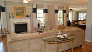 A living room with a beige sofa, a glass coffee table, a fireplace, and a dining area in the background. - Lake Life Escape - The Point on Lake Gaston (Henrico)