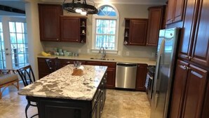 A kitchen with a marble island, wooden cabinets, stainless steel appliances, and a window providing natural light. - Lake Life Escape - The Point on Lake Gaston (Henrico)