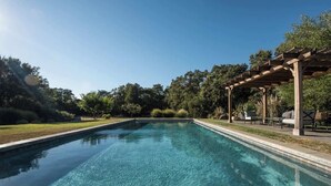 Une piscine rectangulaire à l’eau d’un bleu limpide, entourée d’une pergola en bois et de mobilier d’extérieur.