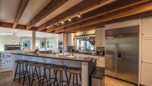 Une cuisine moderne dotée d’un grand îlot central, de tabourets de bar, d’appareils électroménagers en acier inoxydable et de poutres en bois au plafond.