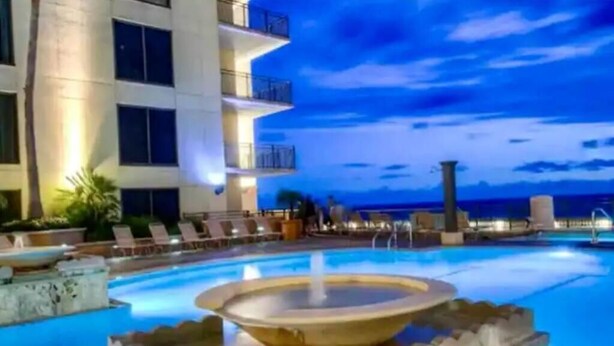 A pool area with a fountain, lounge chairs, and a building with balconies. - Costal Condo - Ocean & Pool Views - Sleeps 6 (Panama City Beach)