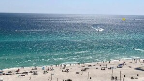 A beach with people sunbathing and swimming, and a parasail in the distance. - Costal Condo - Ocean & Pool Views - Sleeps 6 (Panama City Beach)