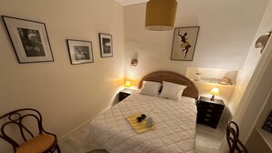 Une chambre à coucher bien rangée, avec un grand lit, deux tables de chevet avec des lampes, une chaise et des tableaux encadrés accrochés au mur.