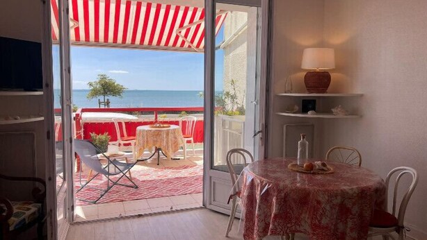 Une pièce avec vue sur la mer, un coin repas avec une table et des chaises, et un auvent à rayures rouges.