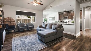 A spacious living room with a gray sectional sofa, a ceiling fan, and a large window overlooking a backyard. - Cal King Hi-tech Vaca Pool Home | Ideal 4 Families (Chico)