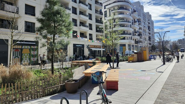 Een moderne straat in de stad met meerlaagsgebouwen, terrassen en een fiets nabij de stoep.