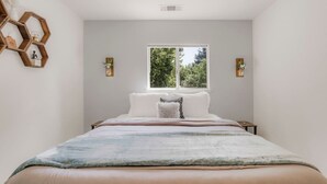 A bedroom with a large bed, a window with a view of greenery, and a geometric wall decoration.