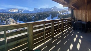 Una terraza de madera con vistas a montañas nevadas y un complejo de esquí.