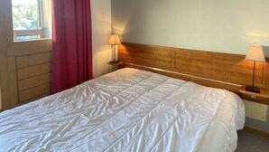 Habitación de hotel con cama, dos lámparas de noche, cabecera de madera, ventana con vistas y cortina roja.