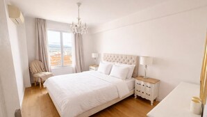 A spacious bedroom with a large bed, a nightstand, a chair, and a view of the city through the window. - Beautiful view Walking distance from the center (Nice)