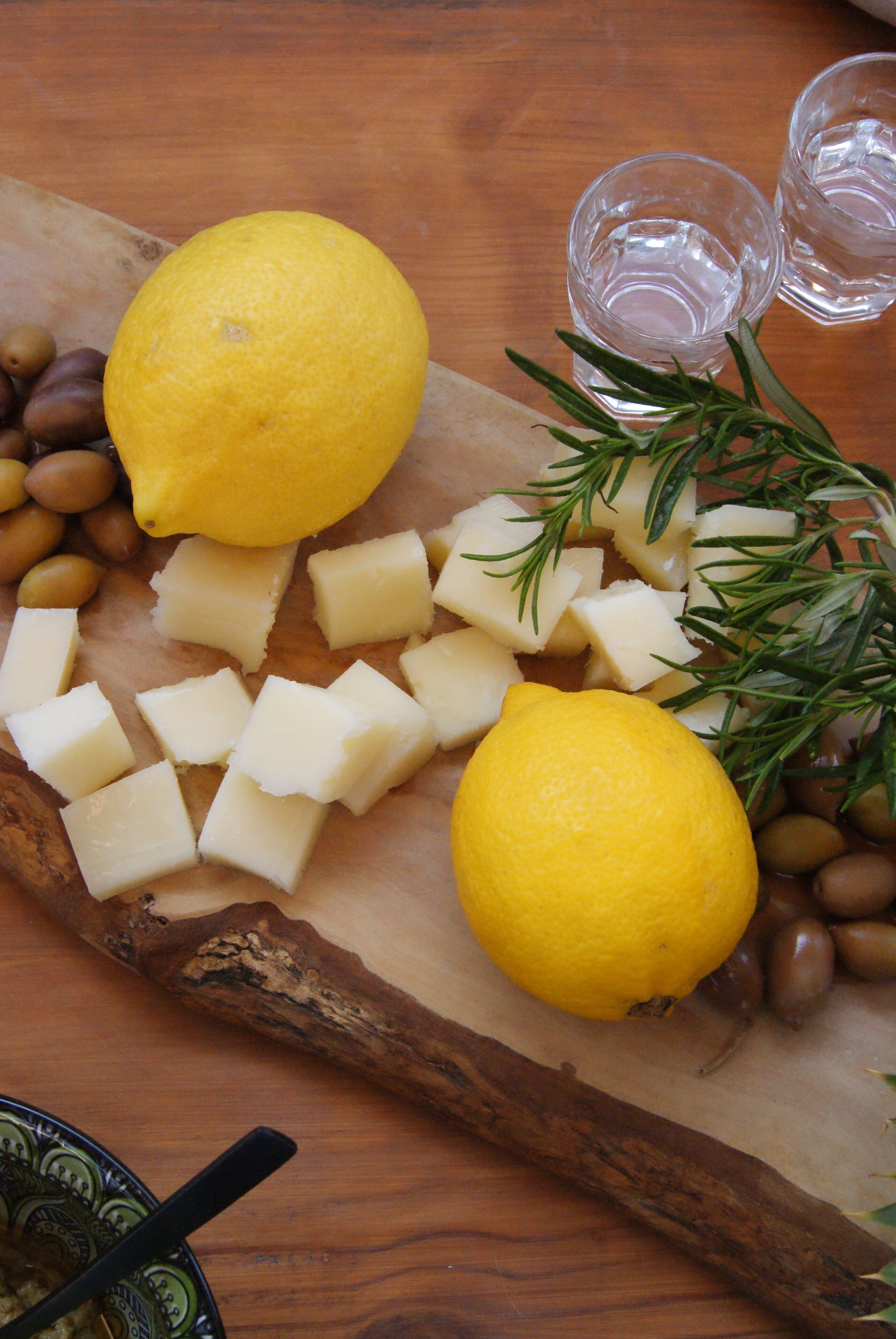 A wooden cutting board with cheese, olives, rosemary, and lemon slices.