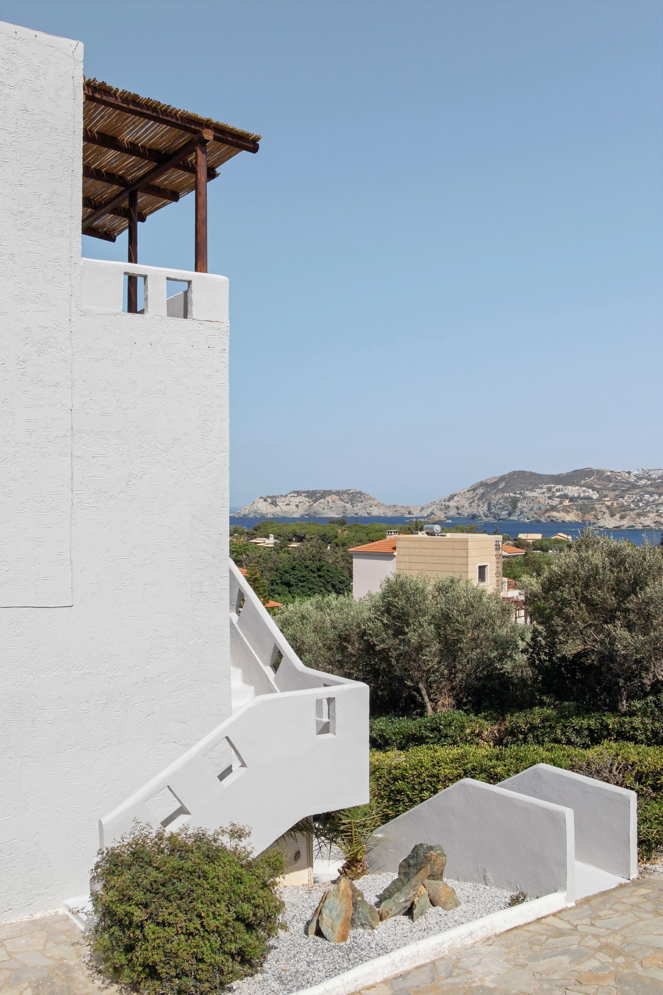 A modern building with a white exterior, a wooden balcony, and a view of a coastal landscape with mountains and a body of water.
