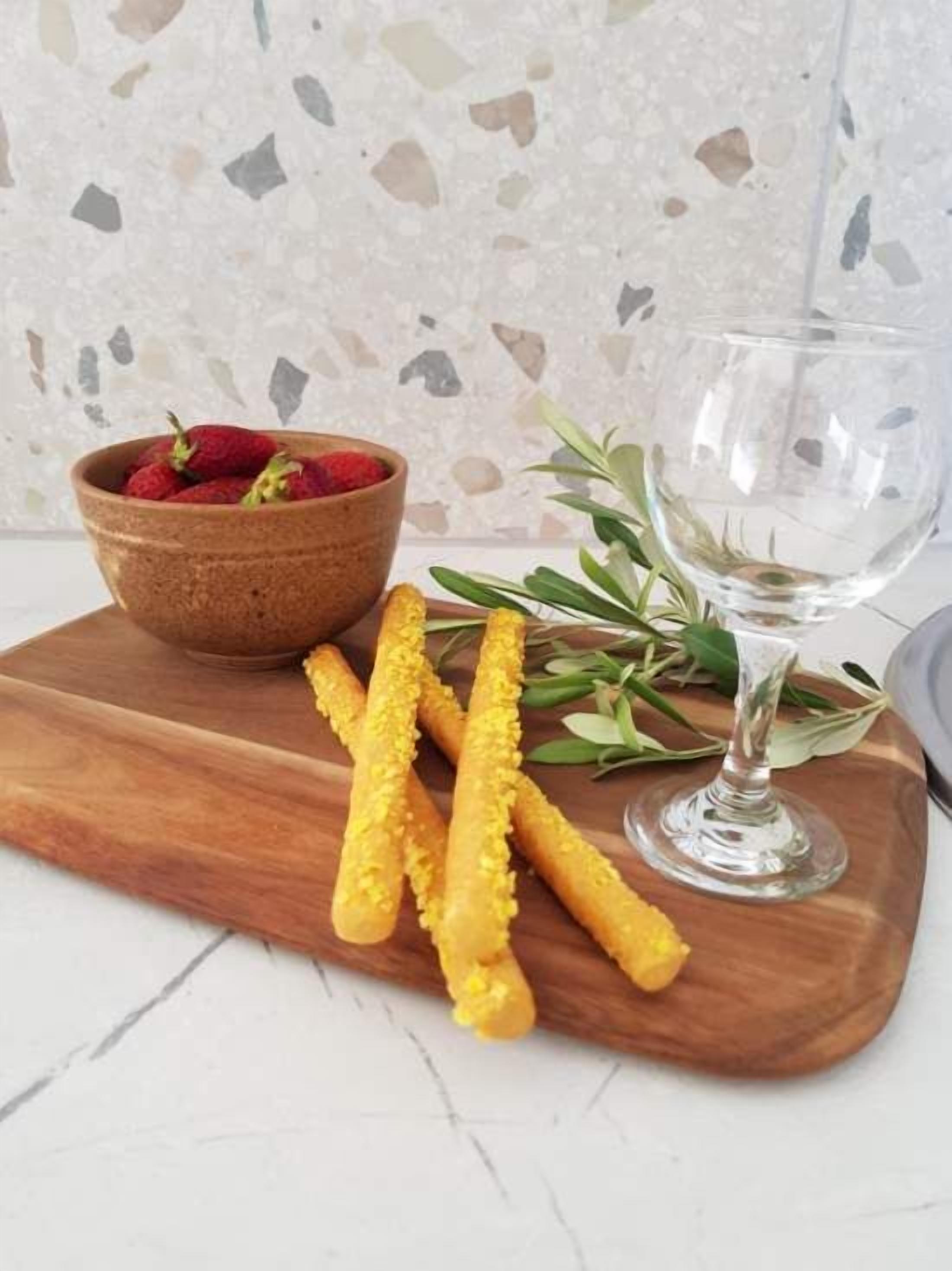 A wooden board with a bowl of strawberries, a glass of water, and some green leaves.