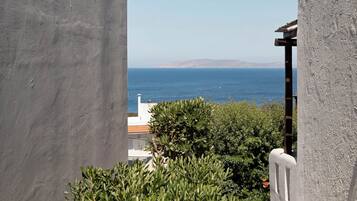 A view of the sea from a balcony with a white railing and a building with a red-tiled roof in the background.