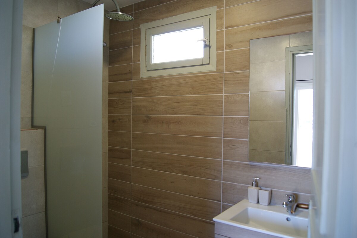 Un baño con paneles de madera, una ventana, un lavabo y una ducha.