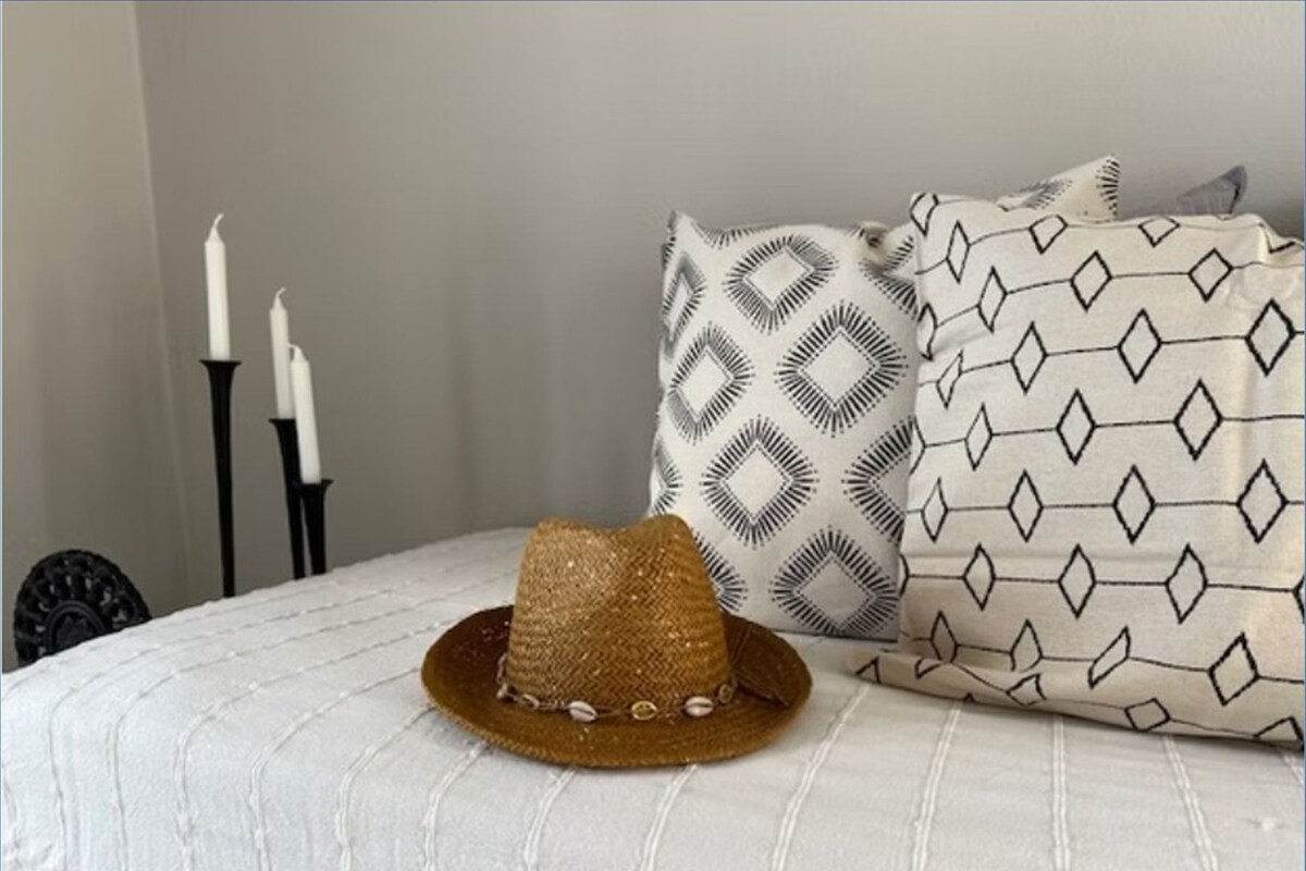 Un lit avec un chapeau de paille, deux chandeliers noirs et des coussins à motifs.