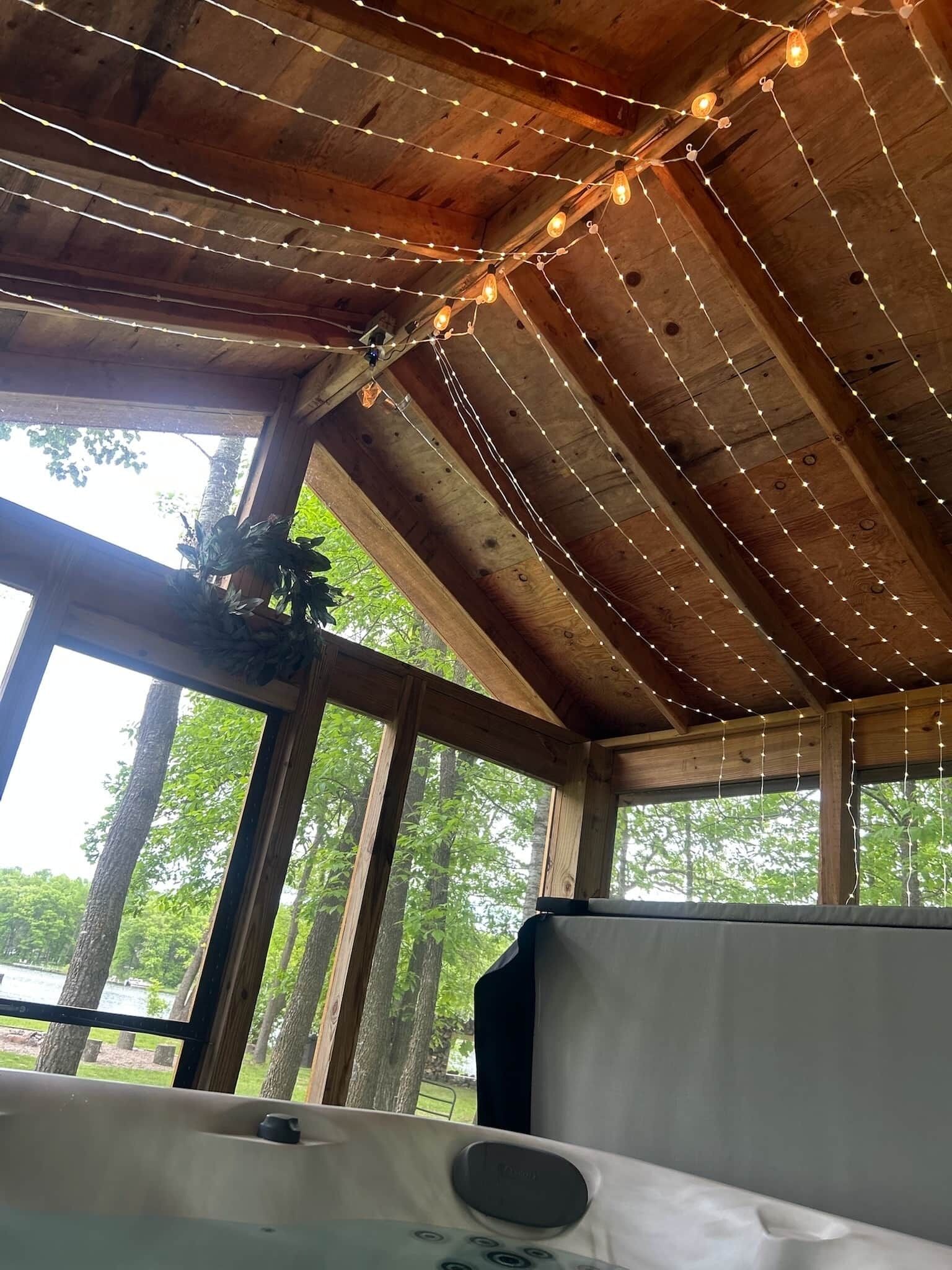 Un intérieur rustique en bois, agrémenté de guirlandes lumineuses, de grandes fenêtres et offrant une vue sur les arbres.