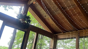 Un interior rústico de madera con luces colgantes, ventanas amplias y vistas a árboles.