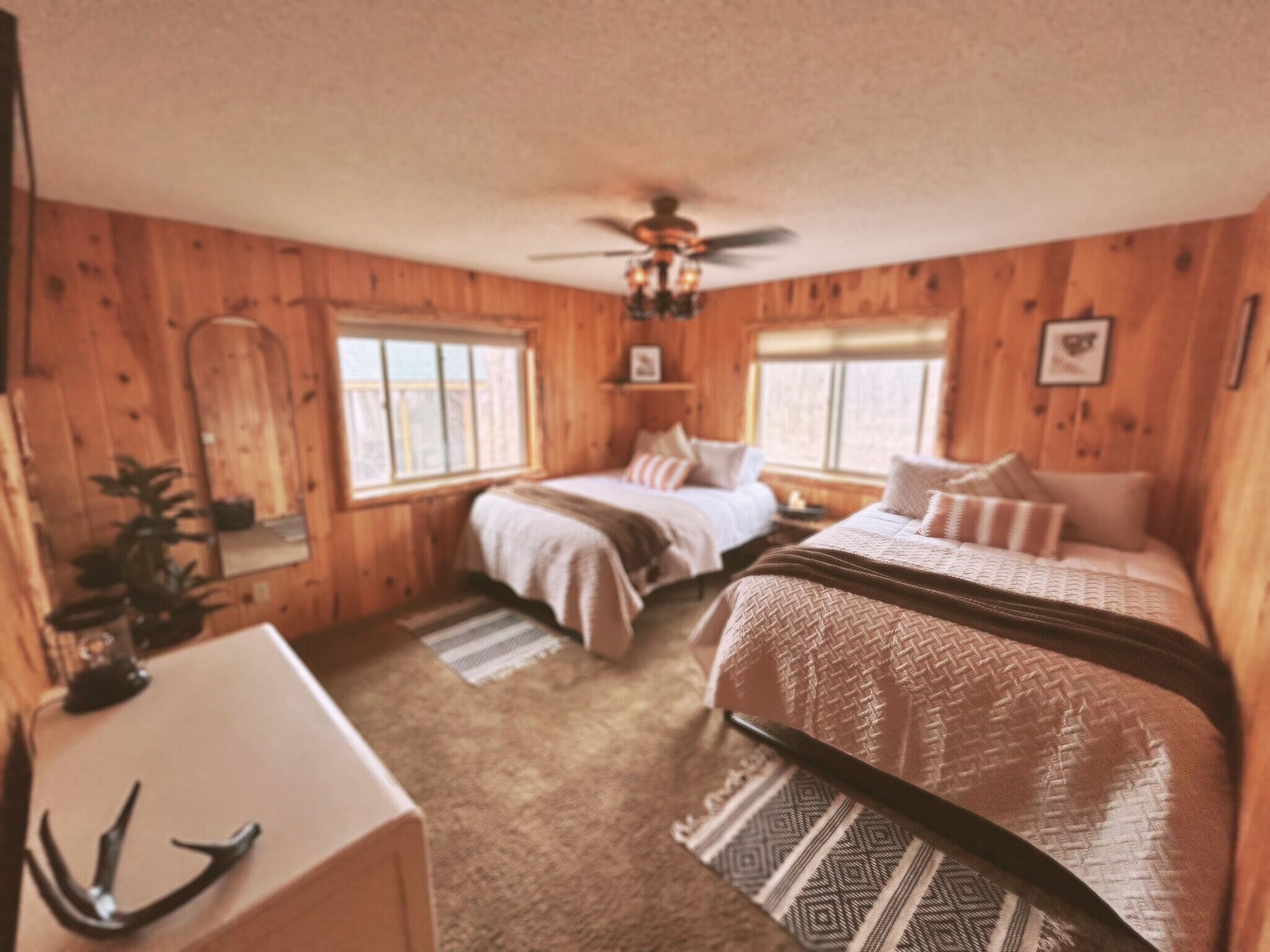 Una habitación acogedora de estilo cabaña con dos camas, un ventilador de techo y paredes de madera.