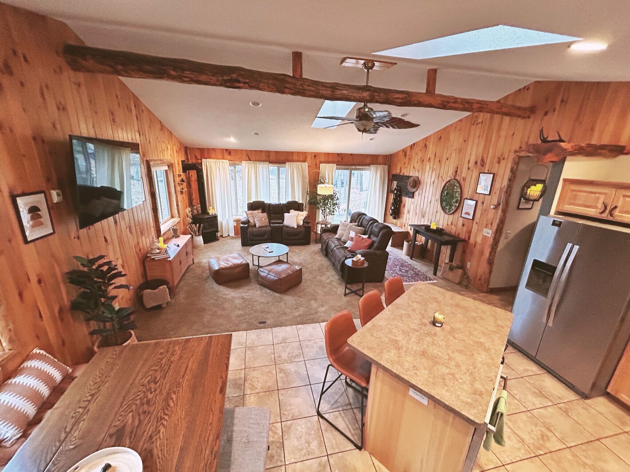 Un intérieur chaleureux de style chalet, avec un revêtement en bois, un coin repas, une cuisine et un salon doté d’une cheminée.