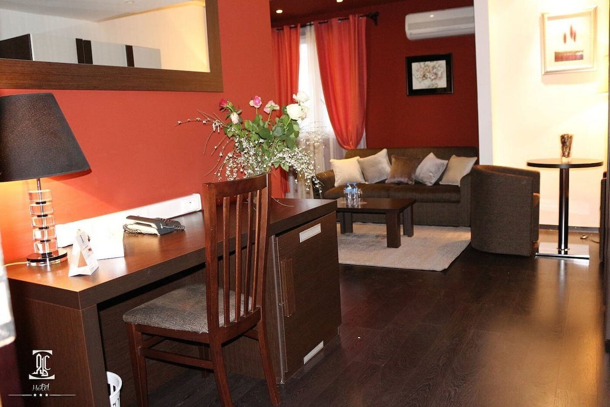 A hotel room with a wooden desk, a chair, a sofa, and a small round table.