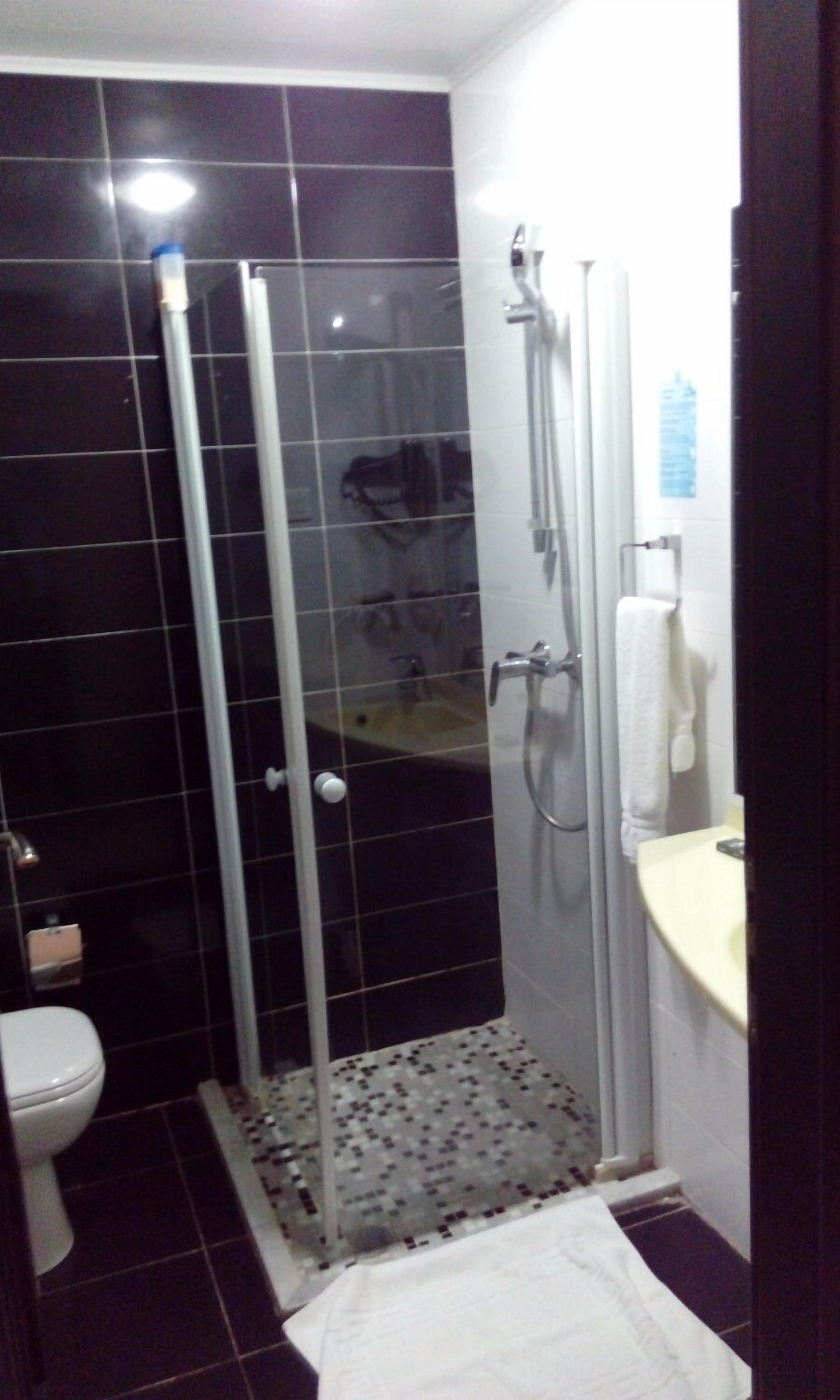 Un baño con ducha envuelta en vidrio, inodoro y lavamanos con una toalla colgada en la pared.
