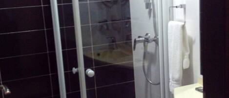 Un baño con ducha envuelta en vidrio, inodoro y lavamanos con una toalla colgada en la pared.