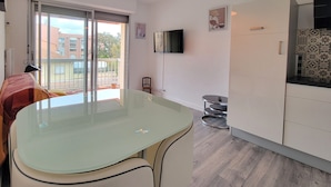 A modern kitchen with a glass-top table, white cabinets, and a TV mounted on the wall. - Charming love nest near the sea (Fréjus)