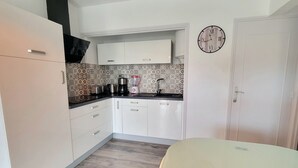 A compact kitchen with white cabinets, a patterned backsplash, and a clock on the wall. - Charming love nest near the sea (Fréjus)