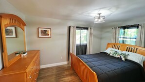 Een slaapkamer met een houten bed, een dressoir, een spiegel en een plafondventilator.