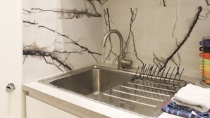 A kitchen with a marble backsplash, stainless steel sink, and a dish rack.