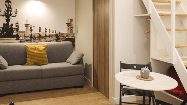 A modern living room with a grey sofa, a small round table, and a staircase.