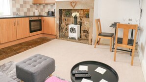 A modern kitchen with wooden cabinets, a stone fireplace, a flat-screen TV, and a dining area with a table and chairs. - Luna Cottage (Holmfirth)