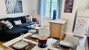 A modern living room with a sofa, dining table set for two, and a kitchen area with a refrigerator. - Lovely flat in the heart of Chamonix (Chamonix-Mont-Blanc)