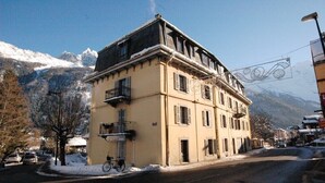 A two-story building with a balcony on the second floor, a sign indicating a cultural center, and a mountain backdrop. - Lovely flat in the heart of Chamonix (Chamonix-Mont-Blanc)