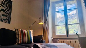 A room with a bed, a window with a view of mountains, a lamp, and a book on the bed. - Lovely flat in the heart of Chamonix (Chamonix-Mont-Blanc)