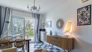A living room with a checkered floor, a sofa, a dining table with chairs, a chandelier, a cabinet, and a large window with curtains. - In the heart of the Cap d'Antibes lovely flat (Antibes)