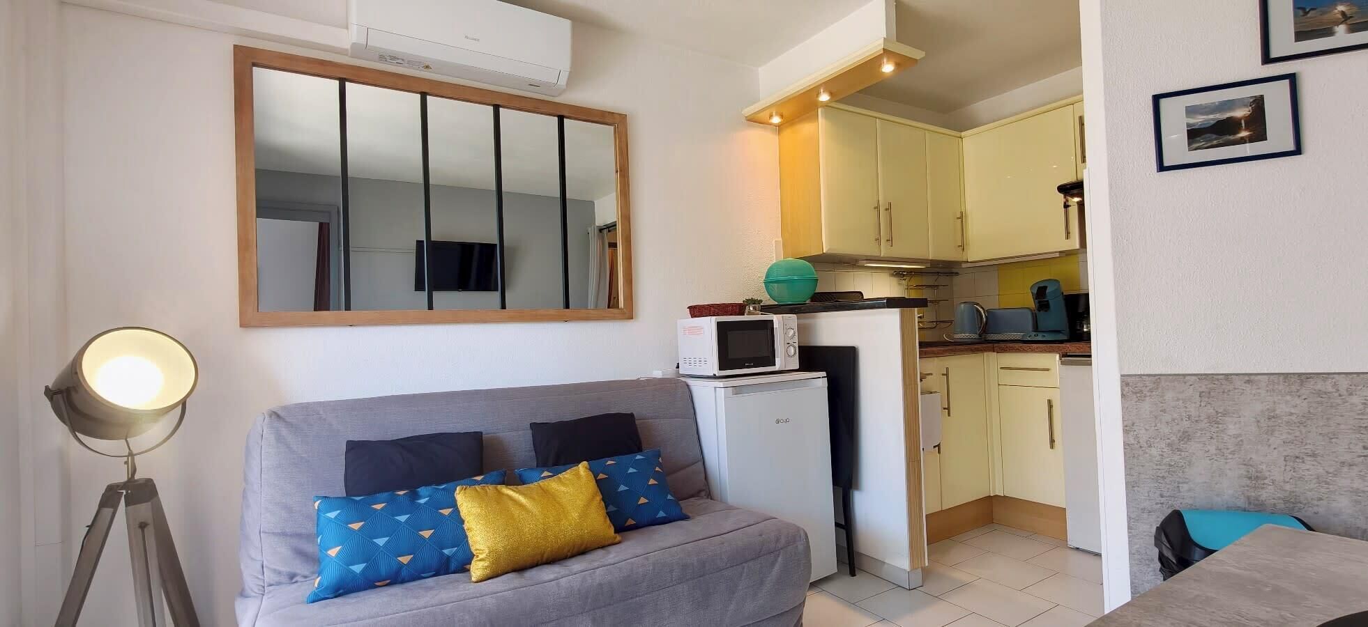 Un espacio habitable compacto con sofá, una kitchenette pequeña, microondas y aire acondicionado instalado en el techo.